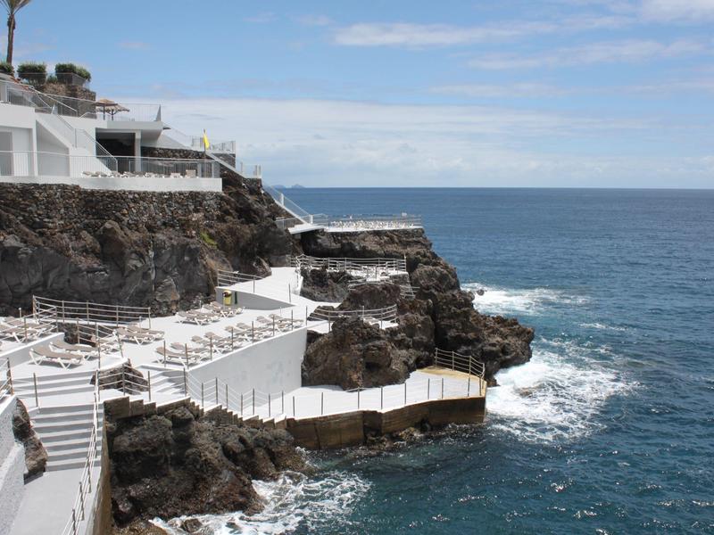 Hotelterrassen und Treppen führen zu einem Steilufer mit Blick auf das blaue Meer.