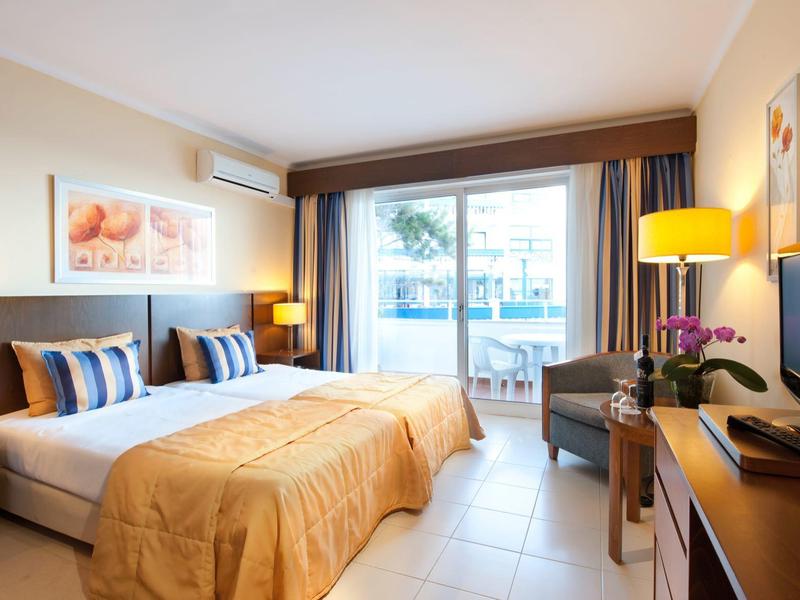 Helles Hotelzimmer mit Doppelbett, Sitzecke und Zugang zu einem Balkon mit Blick.