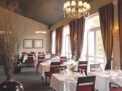 Elegantní restaurace s bílými ubrusy, židlemi, lustr a velkými okny s závěsy.