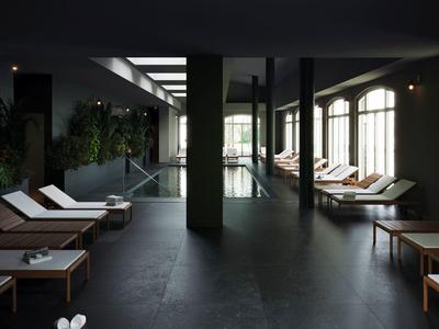 Vnitřní prostor s tmavou podlahou, lehátky a zelenou stěnou vedle bazénu.