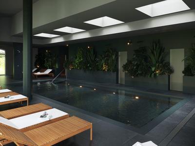 Vnitřní bazén s lehátky a rostlinami, tlumené osvětlení přes stropní otvory.