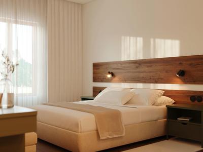 Moderní hotelový pokoj s velkou postelí, dřevěným čelem a světlým kobercem.