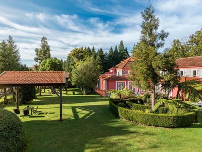 Velká červená budova s upravenou zahradou a zastřešeným posezením pod slunečnou oblohou