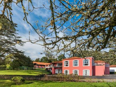 Růžový dům s bílými okny stojí na zeleném trávníku pod modrou oblohou.