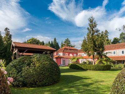 Hotelové budovy s upravenou zahradou a kvetoucími keři pod modrou oblohou.