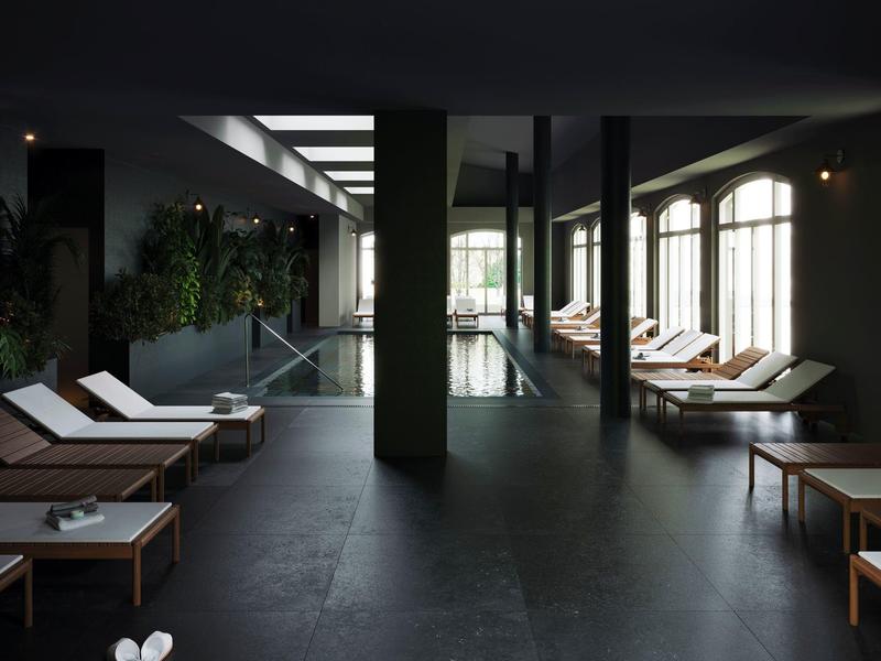 Vnitřní prostor s tmavou podlahou, lehátky a zelenou stěnou vedle bazénu.