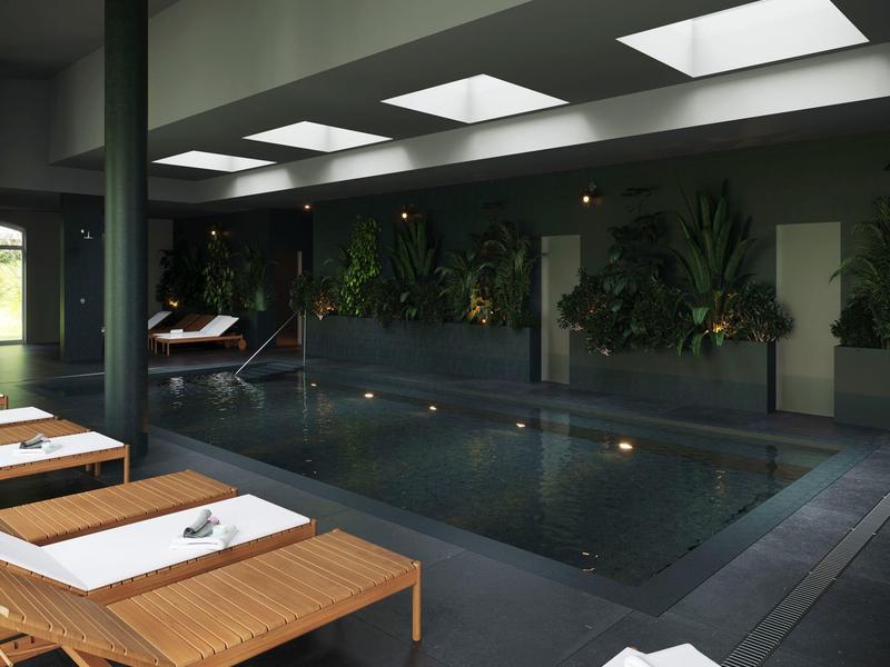 Vnitřní bazén s lehátky a rostlinami, tlumené osvětlení přes stropní otvory.