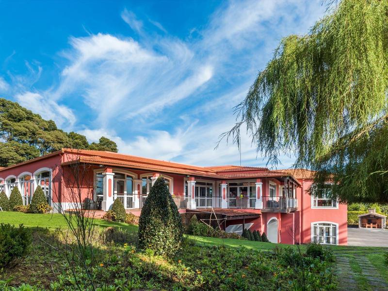 Červená hotelová budova s velkými okny obklopená zelenou krajinou pod modrou oblohou.