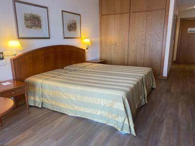 Lichte hotelkamer met groot tweepersoonsbed, houten meubels en warm licht.