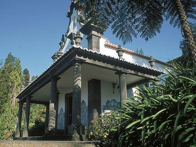 Traditioneel huis met zuilen en overdekt terras, omgeven door bomen en planten.