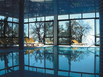 Overdekt zwembad met ligstoelen en grote ramen met uitzicht op bomen buiten.