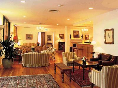 Salon d'hôtel lumineux avec fauteuils confortables, canapés et meubles en bois sur sol en bois.