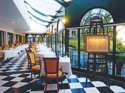 Elegant restaurant met zwart-witte dambordvloer en grote ramen met uitzicht op buiten.