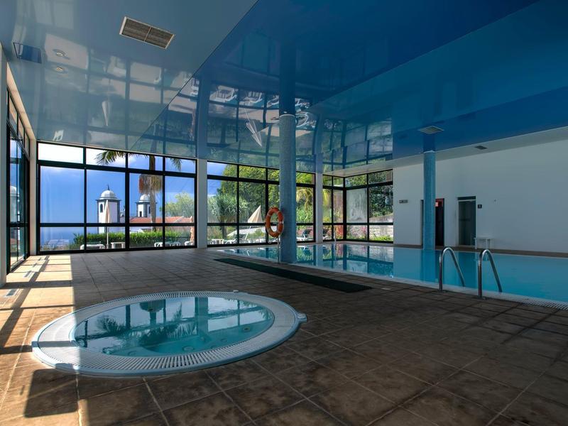 Interieur van hotel met verlicht zwembad en whirlpool, grote ramen met uitzicht op buiten.