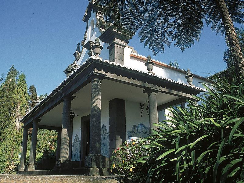 Traditioneel huis met zuilen en overdekt terras, omgeven door bomen en planten.
