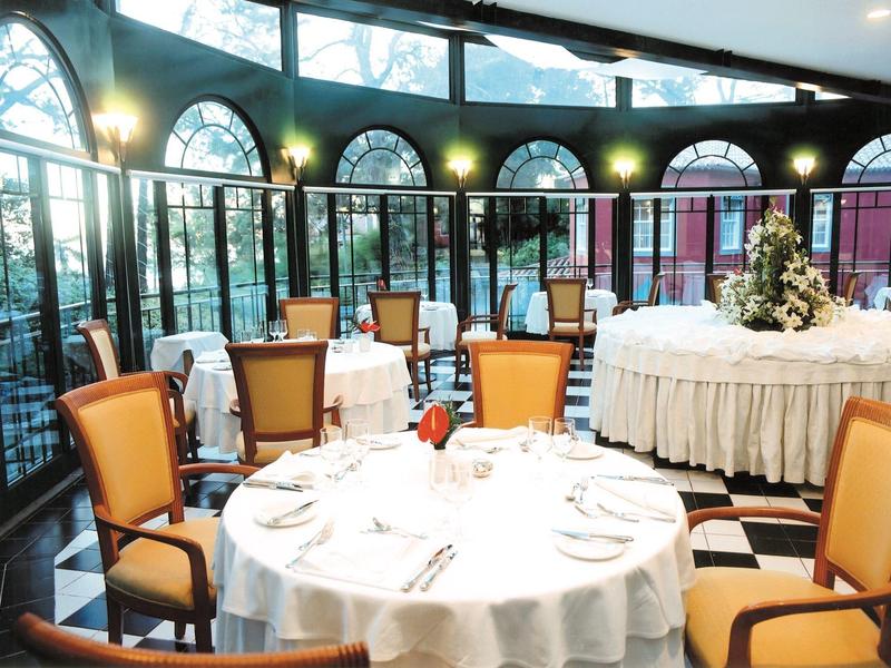 Lichtovergoten serre met ronde, feestelijk gedekte tafels en gele stoelen.