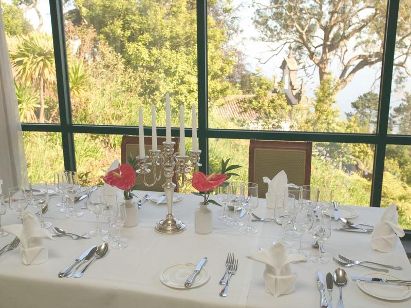 Een elegant gedekte tafel met kandelaars bij grote ramen met uitzicht op groen.