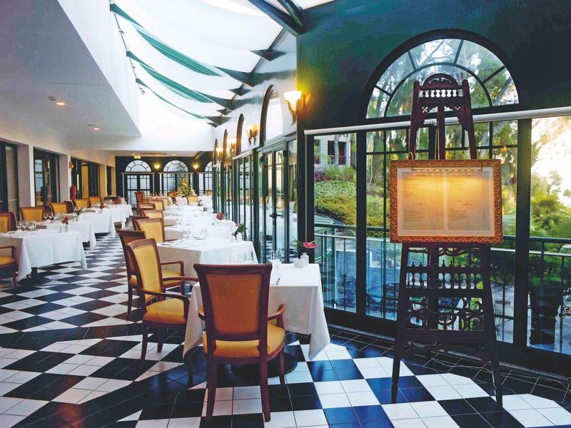 Elegant restaurant met zwart-witte dambordvloer en grote ramen met uitzicht op buiten.