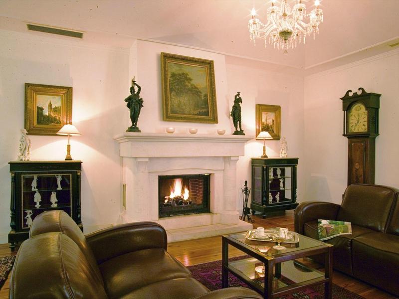 Gezellige woonkamer met leren stoelen, open haard schoorsteen, kroonluchter en antiek meubilair.