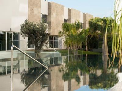 Moderner Pool mit Edelstahl-Geländer, umgeben von Palm- und Olivenbäumen vor hellem Gebäude.