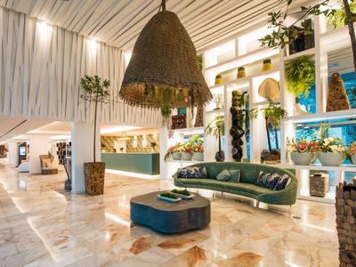 Elegantes Hotelinterieur mit grünem Sofa, Pflanzen und großem Lampenschirm aus Naturmaterialien.