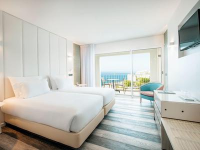 Modernes Zimmer mit großem Bett, Holzboden, Balkon und Meerblick, hell und minimalistisch eingerichtet.