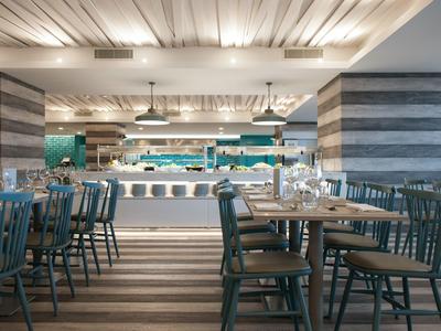 Modernes Restaurant mit Holztischen, grauen Stühlen und heller Deckenbeleuchtung.