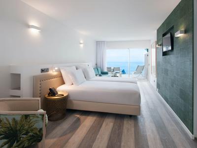 Modern eingerichtetes Schlafzimmer mit großem Bett, Teppichboden und Meerblick durch Fensterfront.