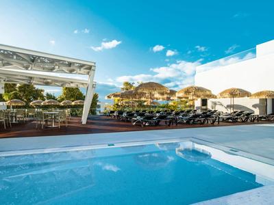 Moderner Außenbereich mit blauem Pool, weißen Liegen, Terrassenmöbeln und Sonnenschirmen.