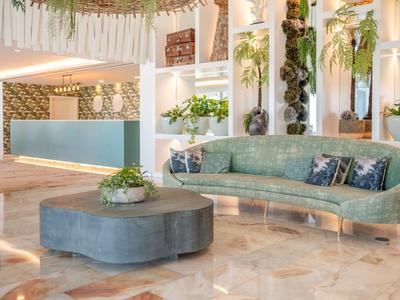 Modernes Hotel-Foyer mit grüner Sitzbank, rundem Tisch, Pflanzen und Marmorfliesenboden.