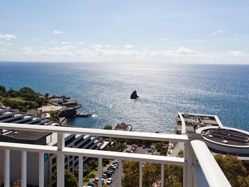 Výhled na moře s bílým balkonem v popředí a částečně oblačnou oblohou.