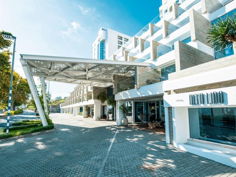 Moderní exteriér hotelu s dlážděnou cestou a bílým přístřeškem.