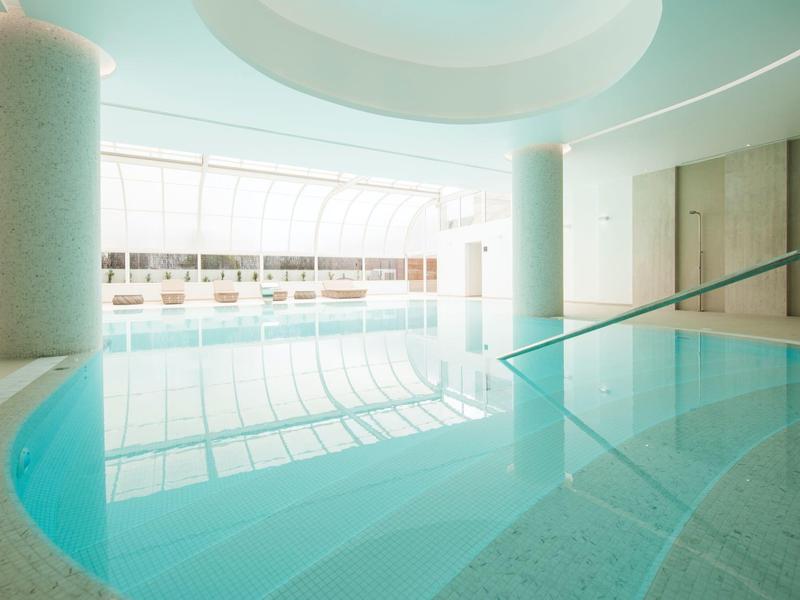 Moderní vnitřní bazén s čistou vodou, velkými okny a dostatkem přirozeného světla.