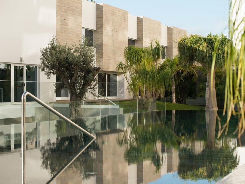 Pokojný bazén obklopený stromy a moderními budovami s hladkými světlými zdmi.