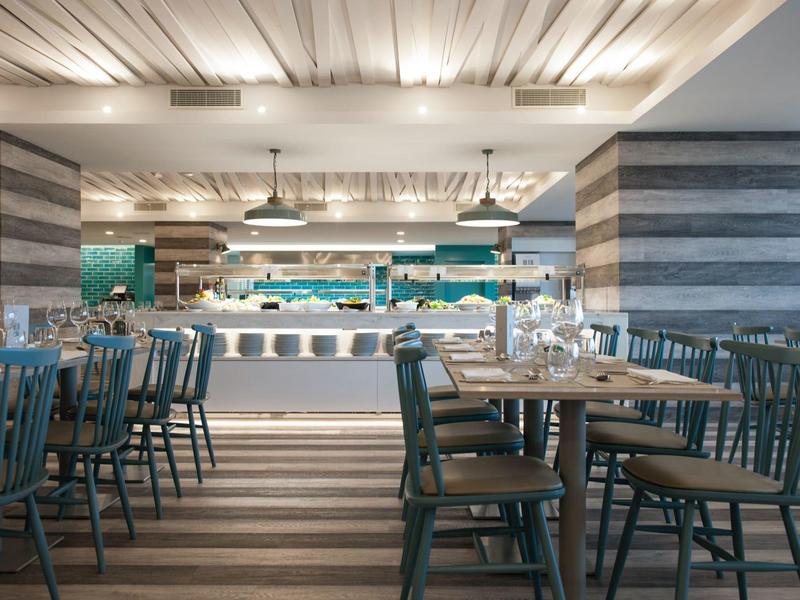 Moderní restaurace s stolky, židlemi a osvětleným servírovacím pultem.