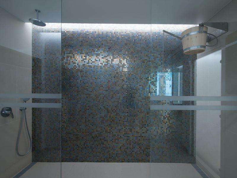 Moderní koupelna se sprchou, obložené stěny a skleněná přepážka.