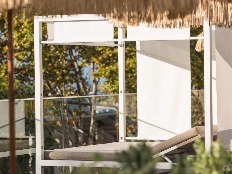 Lehátka pod slámovými slunečníky v venkovní relaxační zóně obklopené zelení.