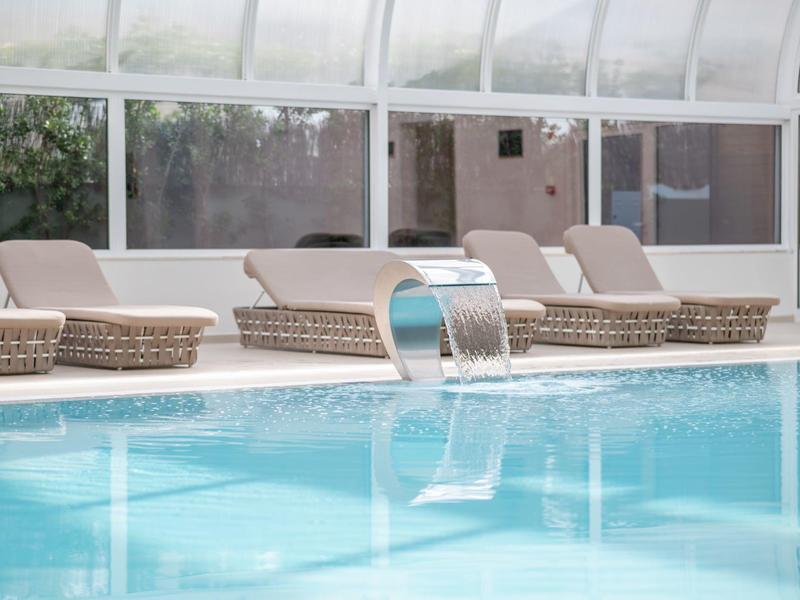 Vnitřní bazén s vodopádem a béžovými ratanovými lehátky.