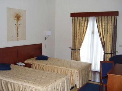 Hotelový pokoj se dvěma jednolůžky, závěsy a květinovým obrazem na stěně.