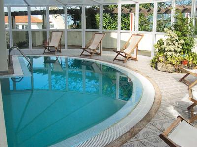 Kruhový vnitřní bazén s lehátky v jasné, zelení prostoupené místnosti.