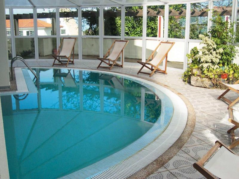 Kruhový vnitřní bazén s lehátky v jasné, zelení prostoupené místnosti.