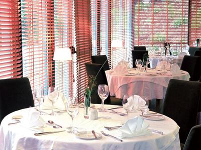 Helles Restaurant mit rund gedeckten Tischen, weißen Tischdecken und schwarzen Stühlen.