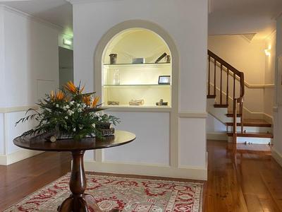 Heller Wohnraum mit Holzfußboden, rotem Teppich, runder Tisch und Blumenarrangement, Treppe im Hintergrund.