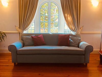 Ein blaugraues Sofa mit roten Kissen vor einem Rundfenster mit hellbraunen Vorhängen.