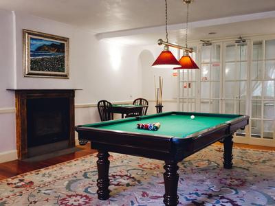 Wohnzimmer mit grünem Billardtisch, Teppich, Kamin und zwei roten Hängelampen an der Decke.