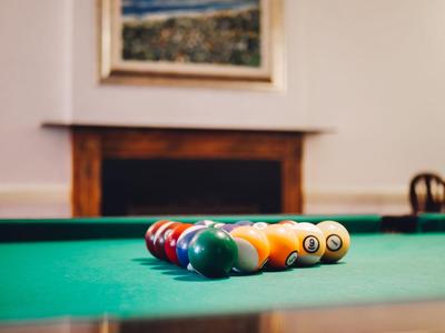 Arrangement of billiard balls in a triangle on a green pool table in front of a fireplace.