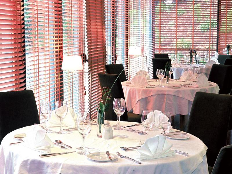 Helles Restaurant mit rund gedeckten Tischen, weißen Tischdecken und schwarzen Stühlen.