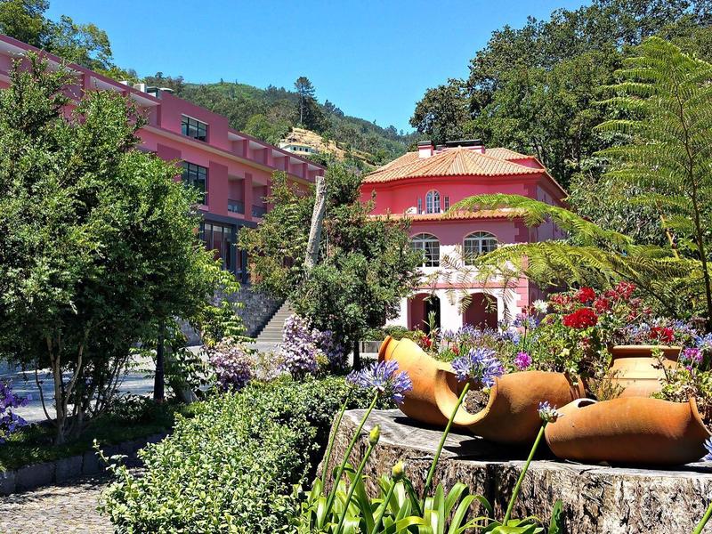 Grüner Garten mit großen Keramikwasserkrügen und einem bunten Pavillon im Hintergrund.