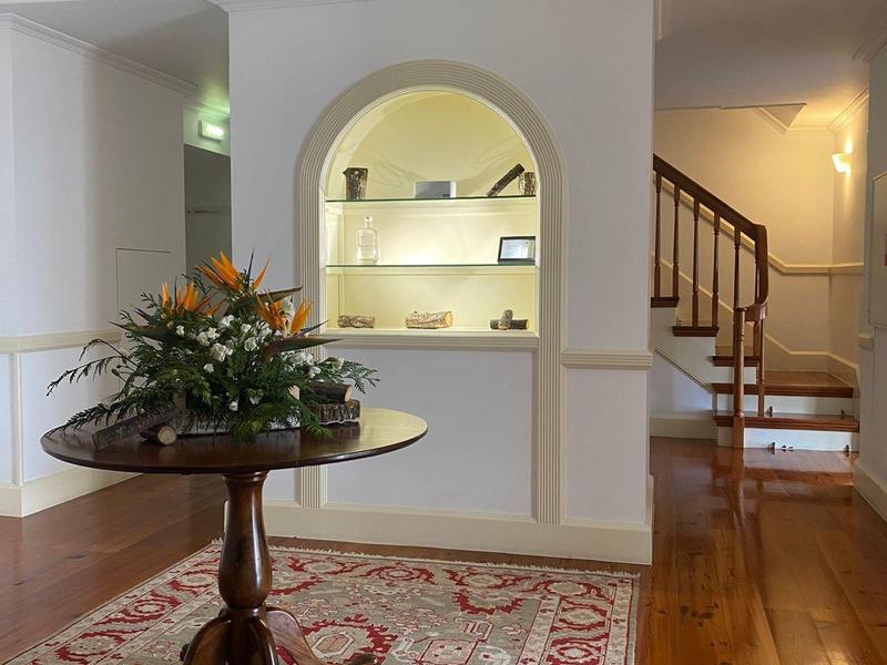 Heller Wohnraum mit Holzfußboden, rotem Teppich, runder Tisch und Blumenarrangement, Treppe im Hintergrund.