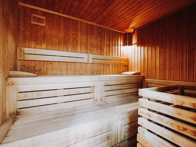 Ein heller Holzsauna-Innenraum mit mehrstufigen Sitzbänken und warmem Licht an der Wand.